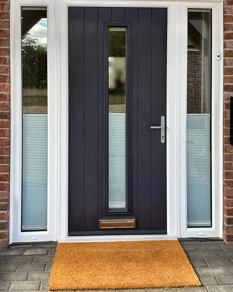 An anthracite grey composite front door with a full-length glass slot, between tall glazed side panels, in red brick.