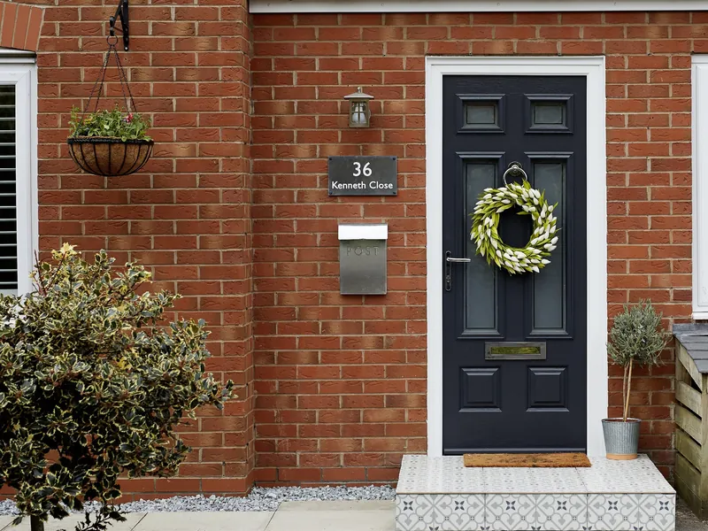 A black panelled Endurance front door with a wreath, in a red-brick wall.