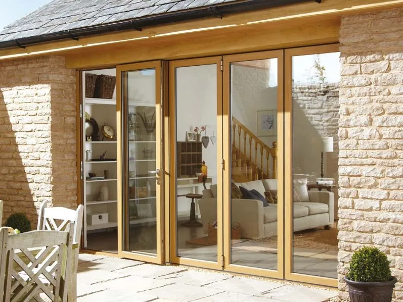 Oak-effect bifold doors folded open in a stone-walled extension, with a living room inside.