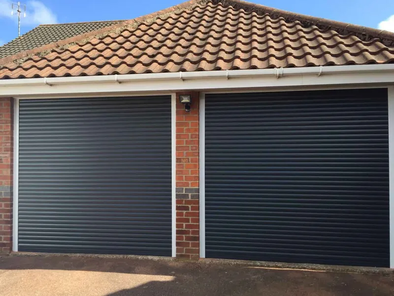Two anthracite grey roller doors on a brick double garage, under a tiled roof.